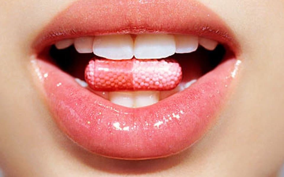 close up of womans mouth holding pill between teeth